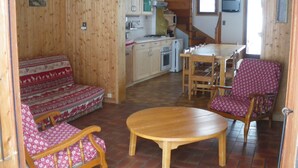 A cozy room with a wooden floor, a sofa with patterned cushions, a wooden dining table, and a chair with a patterned cushion.