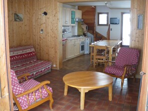 Een gezellige kamer met een houten vloer, een bank met opvallende kussens, een houten eettafel en een stoel met een gestreept kussen.
