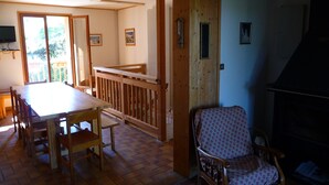 A dining area with a wooden table and chairs, a wooden railing, and a patterned armchair.