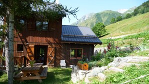 A rustic wooden cabin with a sloped roof, a wooden deck, and a stone wall.