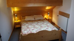 A small, cozy bedroom with a wooden ceiling and a skylight, featuring a single bed with a floral bedspread and two bedside lamps.