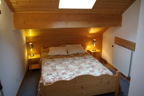 Een kleine, knusse slaapkamer met een houten plafond en dakraam, met een éénpersoonsbed met een bloemenprint beddeken en twee bedlampjes.