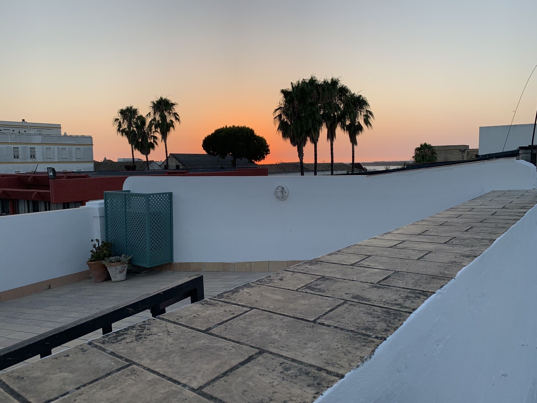 A rooftop terrace with a view of palm trees and a sunset.