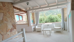 A spacious patio with white wicker furniture, a stone wall, and a view of greenery. - Comfortable apartment with terrace overlooking the sea, near Villasimius (Solanas)