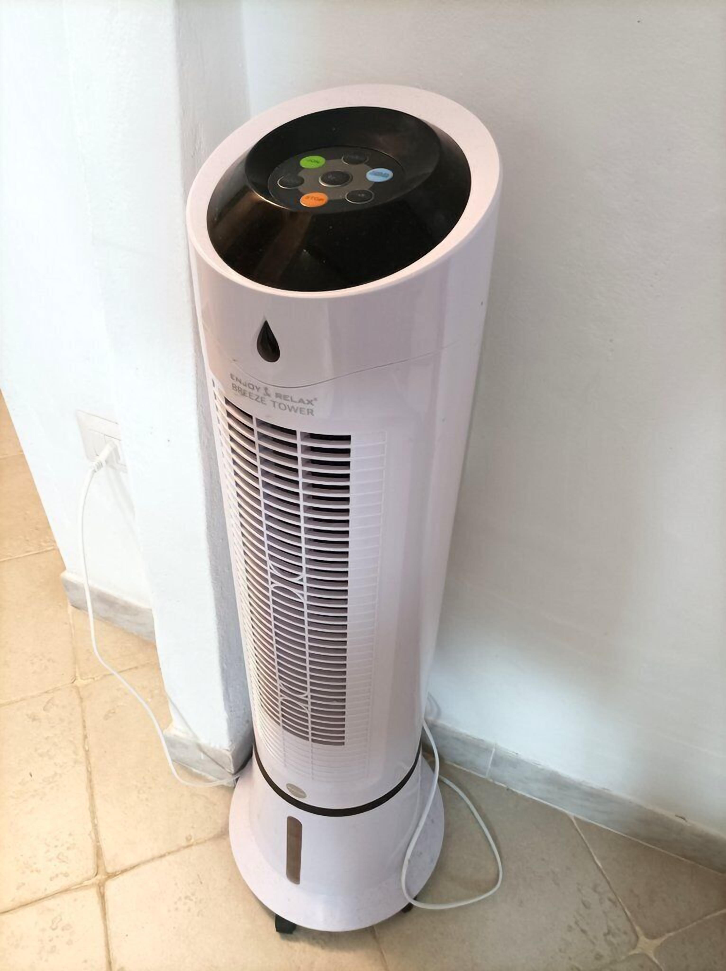 Un climatiseur portatif blanc, doté d’un panneau de commande, est posé sur un sol carrelé, adossé à un mur blanc.