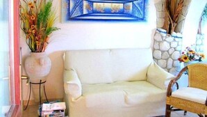 A living room with a white sofa, a coffee table, a patterned rug, a potted plant, and a stone wall. - Comfortable apartment with terrace overlooking the sea, near Villasimius (Solanas)