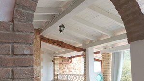 An interior space with a stone archway, a stone wall, a wooden ceiling beam, a stone fireplace, and a white wicker table with chairs. - Comfortable apartment with terrace overlooking the sea, near Villasimius (Solanas)