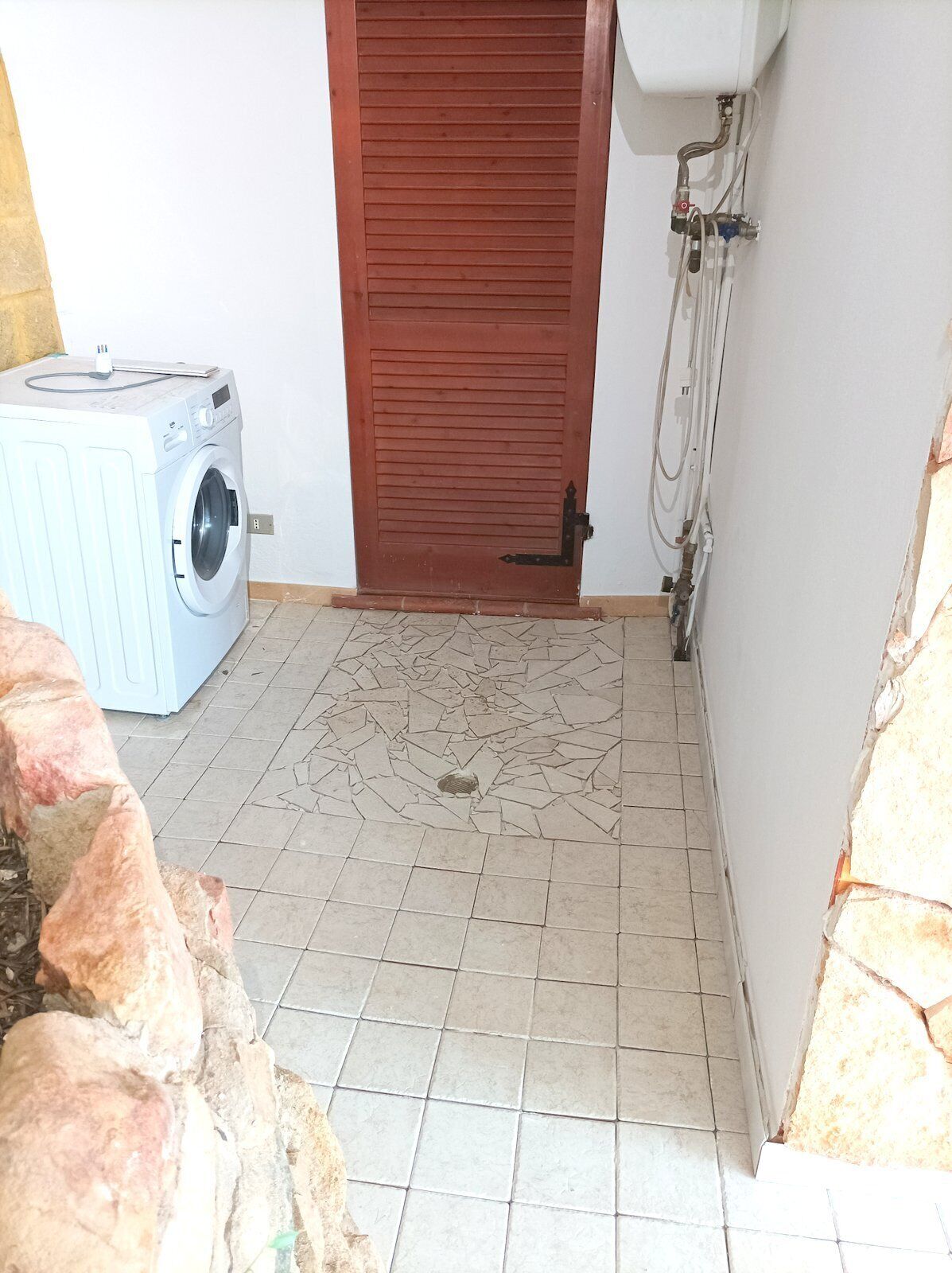A laundry area with a washing machine, a tiled floor, and a wooden door.