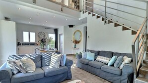 Ein großzügiger Wohnbereich mit zwei grauen Sofas, einem Esstisch mit Stühlen, einem großen Spiegel und einer Treppe.