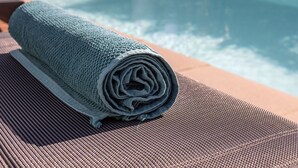 Ein Poolbereich mit gerolltem Handtuch, Liegestühlen und einem Gebäude im Hintergrund.