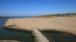 A wide sandy beach with a pier extending into calm waters, a lighthouse in the distance, and a few buildings on the shore. - Breakwater Cottage - Five Bedroom Cottage, Sleeps 10 (Bude)