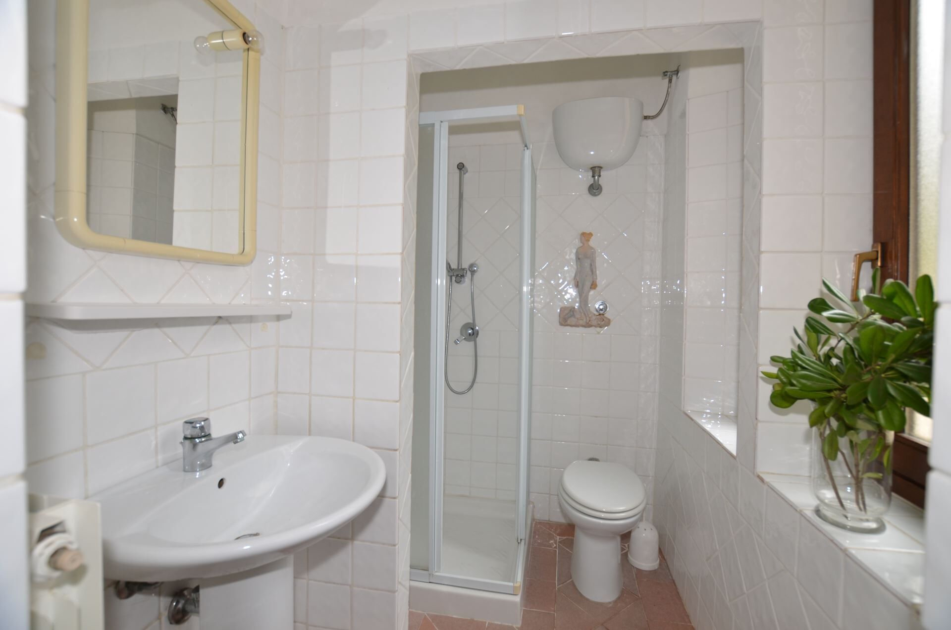 Et badeværelse med vask, toilet, brusebad og et spejl.