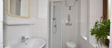 Et badeværelse med vask, toilet, brusebad og et spejl.