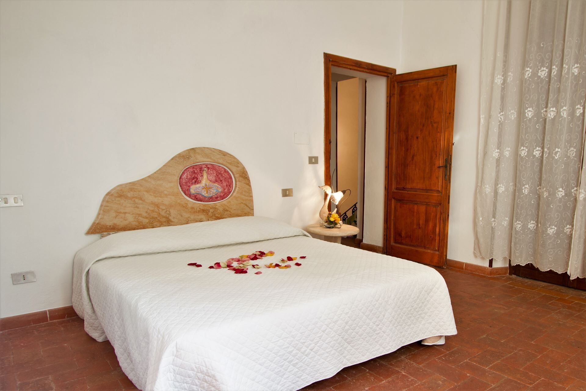 A bedroom with a bed, a wooden headboard, a bedside table with a lamp, and a door.