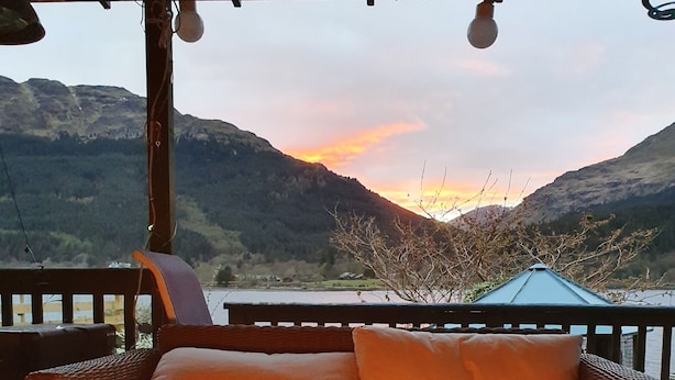A cozy outdoor seating area with a fire feature and a glass of wine, overlooking a mountainous landscape. - Waterfront with Private Hot Tub, Kayaks and Paddleboards free for guests use !!! (ARROCHAR)
