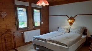 A wooden-paneled bedroom with a bed, a radiator, a hanging light fixture, and a window with a view of the outside. - apartment/ flat - Soultzmatt (Soultzmatt)