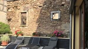 A stone building with a small window and a door. There are three black lounge chairs and potted plants with red flowers. - apartment/ flat - Soultzmatt (Soultzmatt)