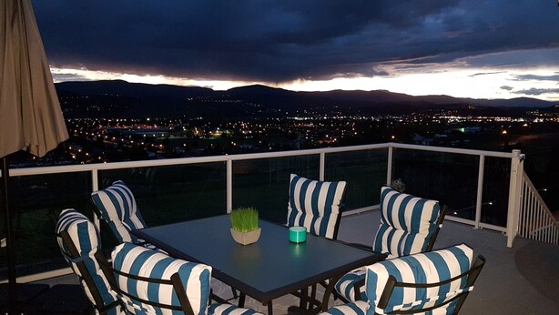 A balcony with a table and chairs, overlooking a cityscape at dusk. - Perfect retreat * LEGAL BNB *  4 rooms on site. Group bookings available. (Kelowna)