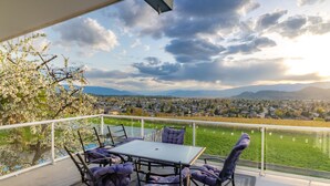 A balcony with a table and chairs, overlooking a cityscape and green fields. - Perfect retreat * LEGAL BNB *  4 rooms on site. Group bookings available. (Kelowna)