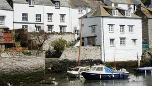 A coastal building with multiple windows, a stone wall, and boats docked in the water.