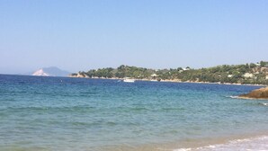 Una playa con aguas cristalinas, orilla de arena y una costa distante con edificios y vegetación.