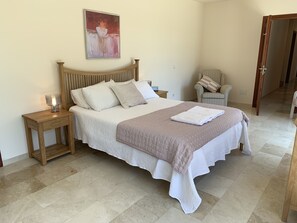 Ein ordentlich eingerichtetes Schlafzimmer mit einem Bett, Nachttischen, einem Sessel und einem Bild an der Wand.
