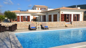 Una piscina con paredes de piedra y un suelo de baldosas, rodeada de sillas de descanso y una mesa.