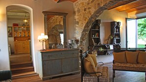 A rustic interior with a stone archway, wooden furniture, and a kitchen area visible through an archway.