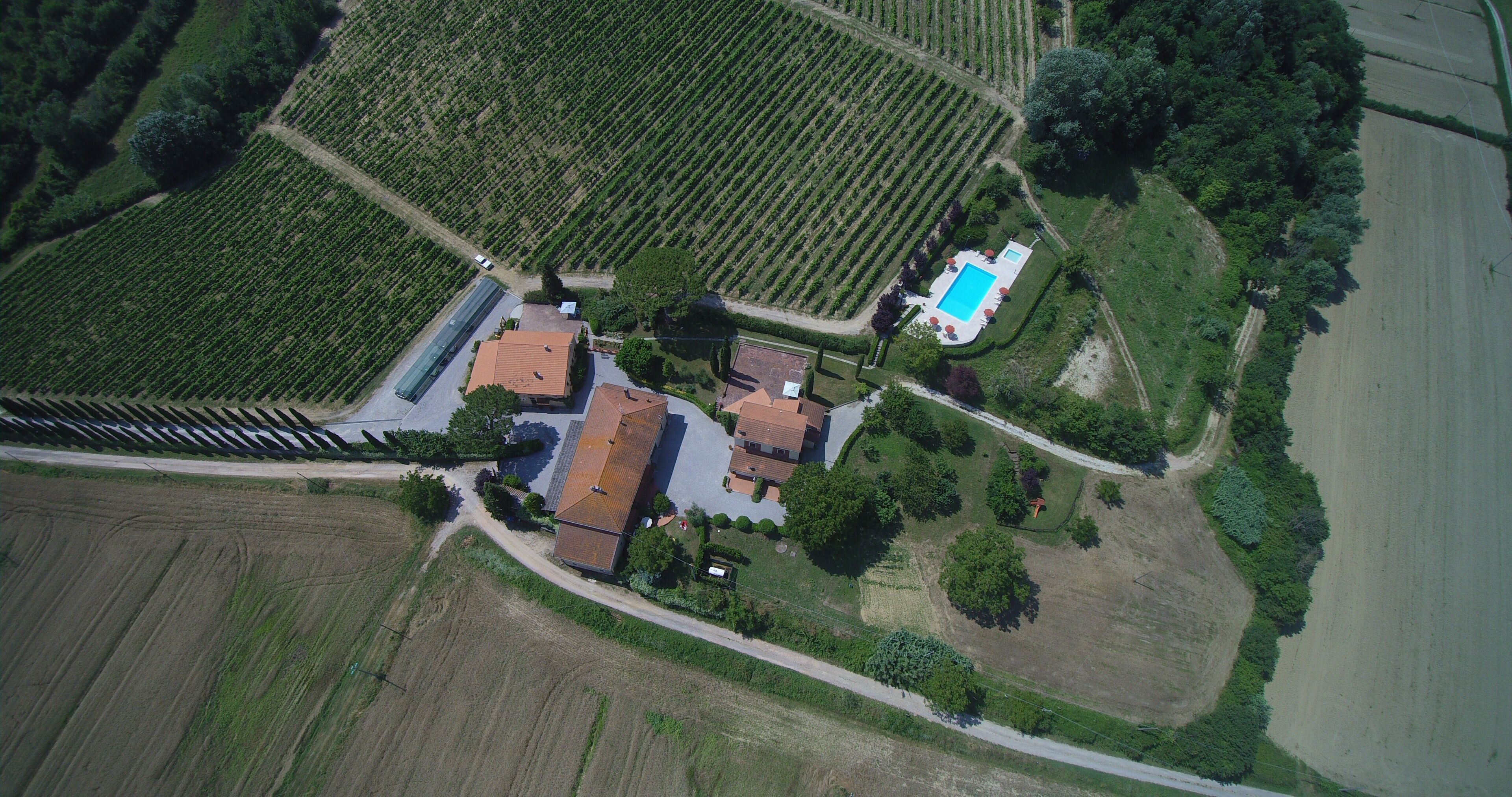 Vista aérea de uma propriedade com piscina, vários edifícios e campos agrícolas ao redor.