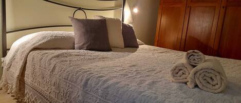 A neatly made bed with a patterned blanket and pillows, a wooden wardrobe, and a small bedside lamp.