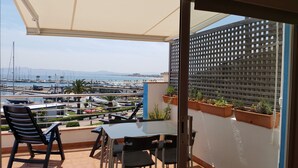 Un balcón con mesa y sillas, con vista a un puerto deportivo con barcos y una playa.