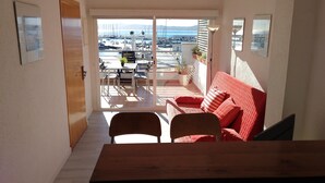 Un balcón con un sofá rojo, una mesa de madera y vistas a barcos y un puerto deportivo.