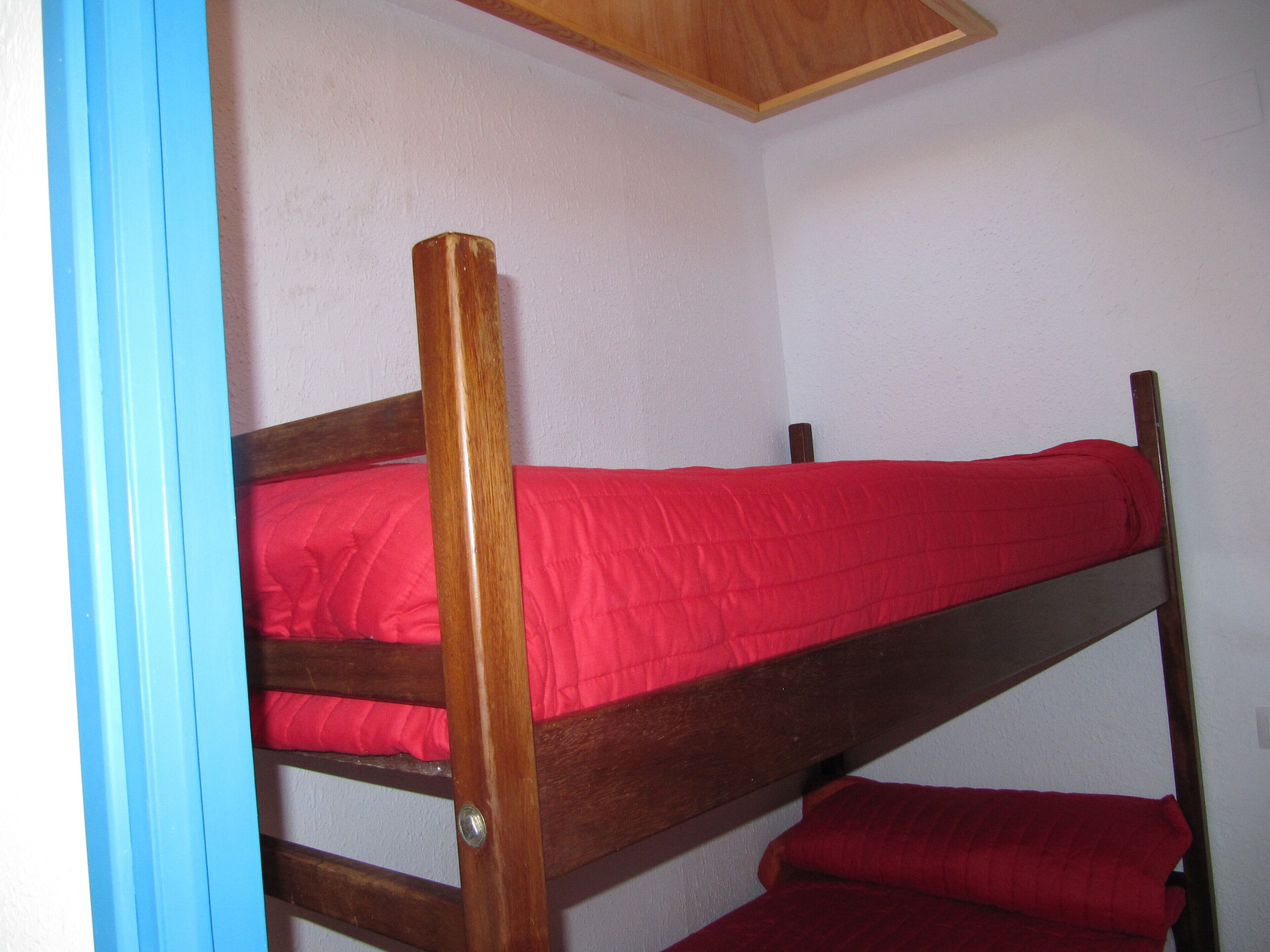 Una cama litera con ropa de cama roja en una habitación con paredes blancas y techo de madera.