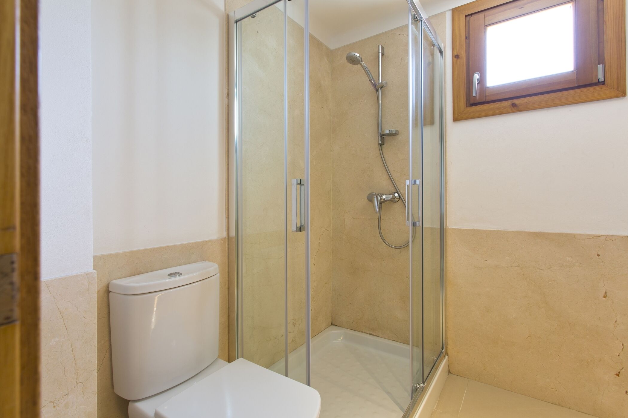 A bathroom with a glass-enclosed shower, a toilet, and a window.