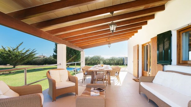 A covered patio area with wicker furniture, a dining table, and a view of a swimming pool and greenery. - Ca Na Volantina - Great family villa close to Puerto Pollensa (Port de Pollença)