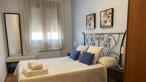 A neatly made bed with a white bedspread and blue pillows, a bedside table with a lamp, and a window with sheer curtains. - Casa Lola Beceite Apartments, mountain views and petfriendly (Beceite)
