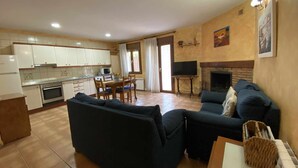 A living room with a sofa and a TV, a kitchen with cabinets and a stove, and a fireplace. - Casa Lola Beceite Apartments, mountain views and petfriendly (Beceite)