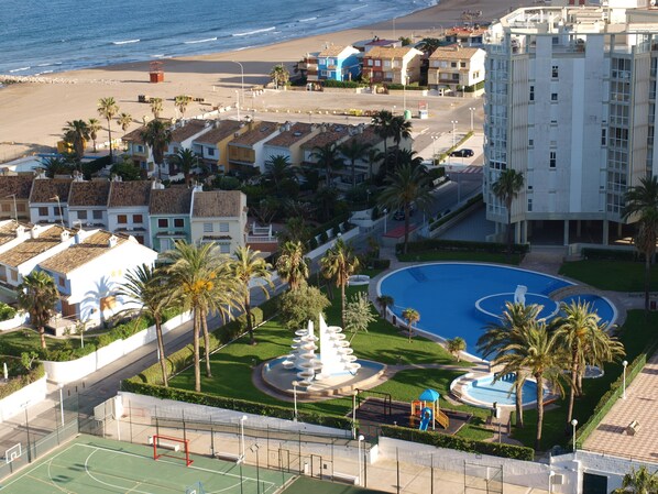 A coastal hotel with a swimming pool, tennis court, and a view of the beach.