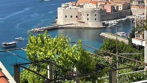 A coastal cityscape with historic buildings, a fortified structure, and a marina with boats. - Studio Apartment Klara  Breathtaking view to the sea and Old Town! (Dubrovnik)