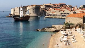 A coastal town with a historic fort, clear blue waters, and a sandy beach with sun loungers. - Studio Apartment Klara  Breathtaking view to the sea and Old Town! (Dubrovnik)