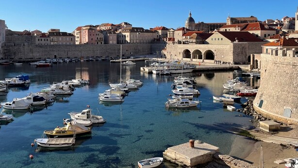 A historic harbor with numerous boats docked, stone walls, and a prominent building with arches. - Studio Apartment Klara  Breathtaking view to the sea and Old Town! (Dubrovnik)