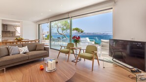 Un salon moderne doté d’un grand téléviseur, d’un canapé et d’un coin repas offrant une vue sur la mer.