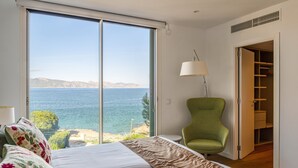 Une chambre avec une grande porte-fenêtre coulissante donnant sur la mer, un fauteuil vert et un dressing.