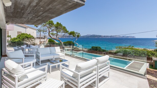 Une terrasse extérieure moderne, avec des meubles blancs, une piscine et une vue sur la mer.