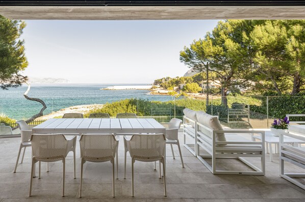 An outdoor patio with a table and chairs, overlooking a coastal landscape with trees and a view of the sea.