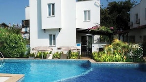 A modern building with a swimming pool, a covered outdoor seating area, and lush greenery.