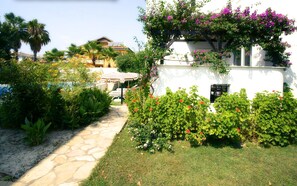 Eine Villa mit einer privaten Terrasse und einer schattigen Sitzecke, umgeben von üppiger Bepflanzung und blühenden Pflanzen.