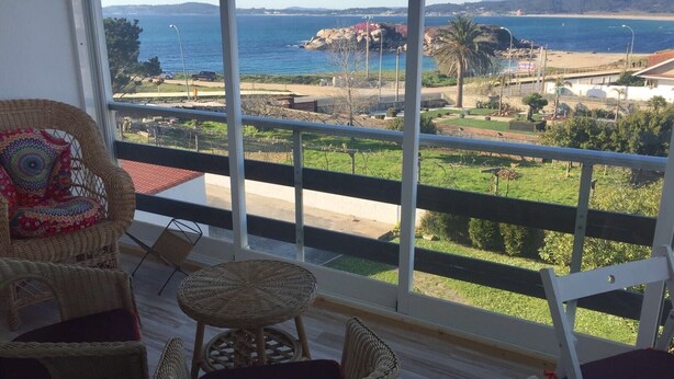 Un balcón con mobiliario de mimbre, vista al mar y una playa distante.