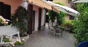Eine Terrasse mit Tisch und Stühlen, einem Blumentopf und einem weißen Sonnenschirm.