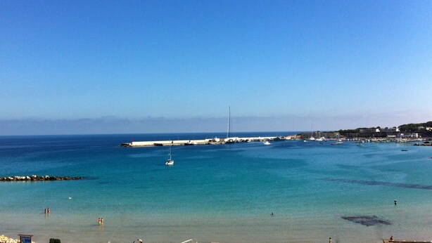 A coastal view with a pier extending into the sea, boats, and a clear sky.